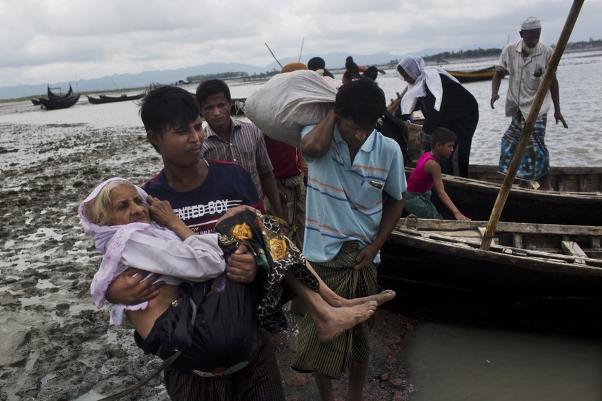 A Rohingya ethnic minority from Myanmar carries an elderly woman as they alight from a local boat on which they crossed a river, after crossing over to the Bangladesh side of the border near Cox&#039; ...