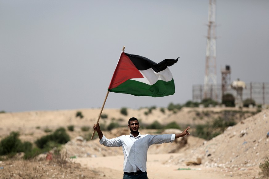 epa06109048 A Palestinian protester waves a Palestinian flag next to the Israeli control military tower during a Hamas protest against the security measures at the al-Aqsa mosque, near the border betw ...