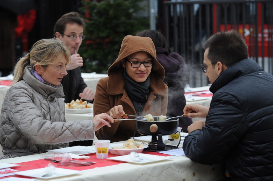 Leute geniessen ein warmes Kaesefondue auf der Piazza Manzoni in Lugano am Samstag, 21. Dezember 2013. (Ti-Press/Davide Agosta)