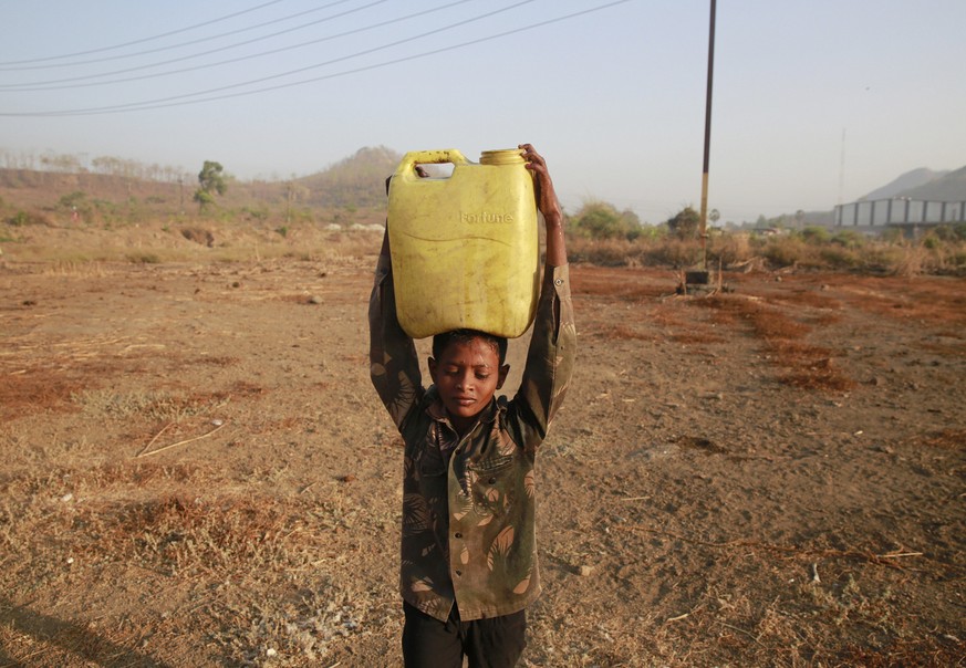 In this April 12, 2016 photo, a boy who migrated from drought hit areas of the western Indian state of Maharashtra, carries water to his family's makeshift hut in Kukse Borivali, 85 kilometres (5 ...