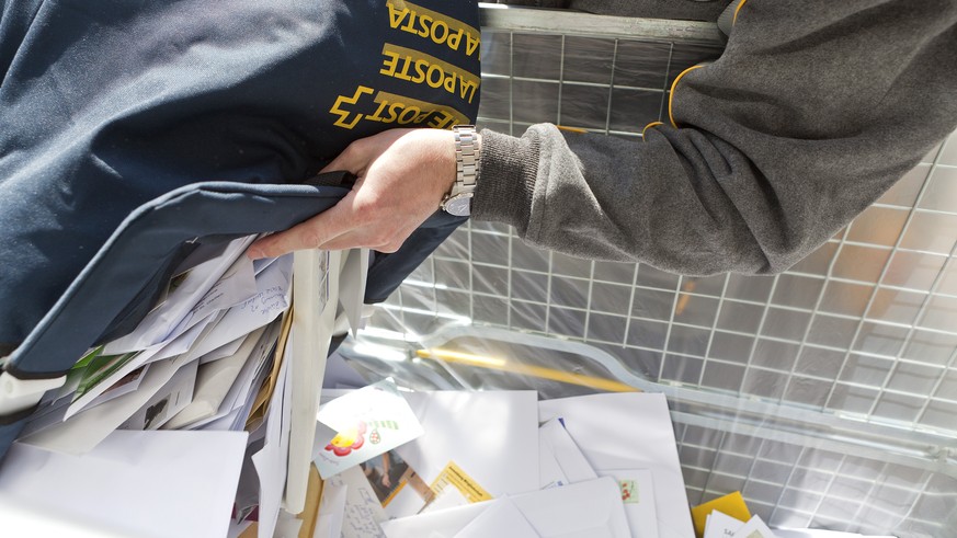 ZUM HALBJAHRESERGEBNIS 2015 DER SCHWEIZERISCHEN POST STELLEN WIR IHNEN FOLGENDES THEMENBILD ZUR VERFUEGUNG - An employee of the Swiss Post empties a bag full of letters and cards into a bin on his mai ...