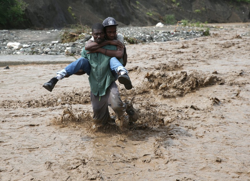 epaselect epa05572083 A group of people try to cross the river La Digue, after the colapse of the only bridge that connects to the south after the passing of hurricane Matthew in the country, in Petit ...