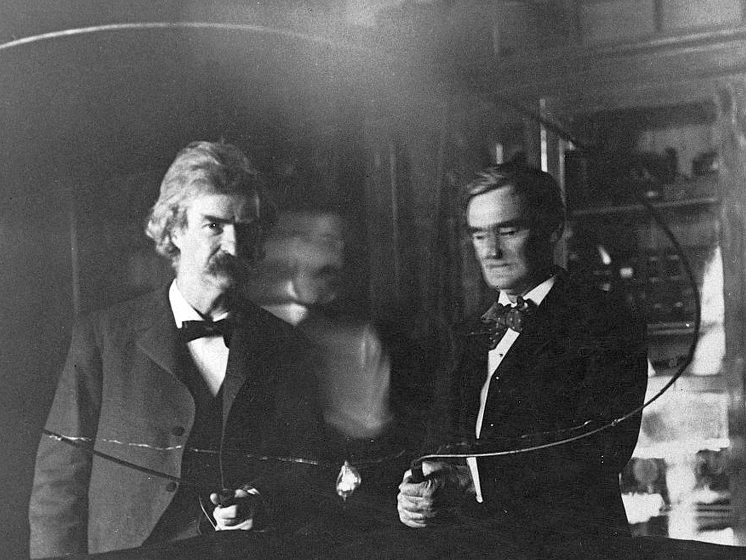 Nikola Tesla (verschwommen im Hintergrund) leitet Strom durch seinen Bewunderer – den amerikanischen Schriftsteller Mark Twain – und den Schauspieler Joseph Jefferson (rechts), um eine Glühbirne zum L ...