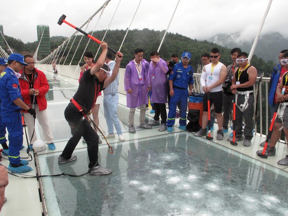 A man strikes a hammer against a 430-meter-long glass-bottom bridge during a safety test ceremony, in Zhangjiajie, Hunan province, China, June 25, 2016. Picture taken June 25, 2016. REUTERS/Jimmy Guan