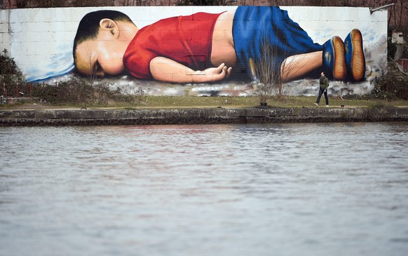 epa05206149 The photo of the dead Syrian boy Aylan Kurdi served as a template for a graffiti that artists Justus Becker and Oguz Sen sprayed at the harbour in Frankfurt (Main), Germany, 11 March 2016. ...