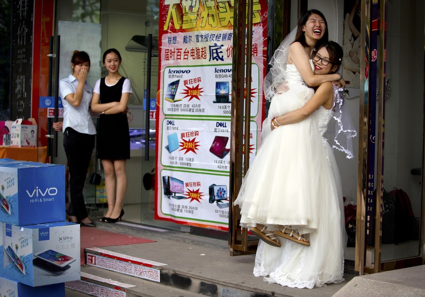 Li Tingting, second from right, laughs as she is lifted off the ground by her wife Teresa Xu, right, outside of a beauty salon where the two were preparing for their wedding as clerks from an adjacent ...