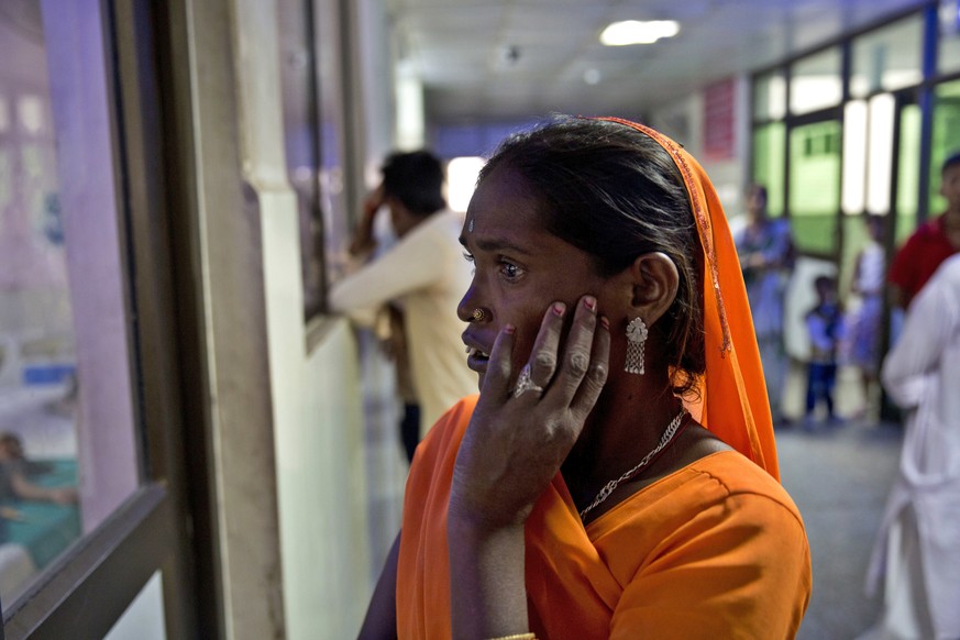 An Indian woman looks through the window glass of the emergency ward for a glimpse of her one and half year old grandson who is under treatment at the Baba Raghav Das Hospital where 35 children died i ...