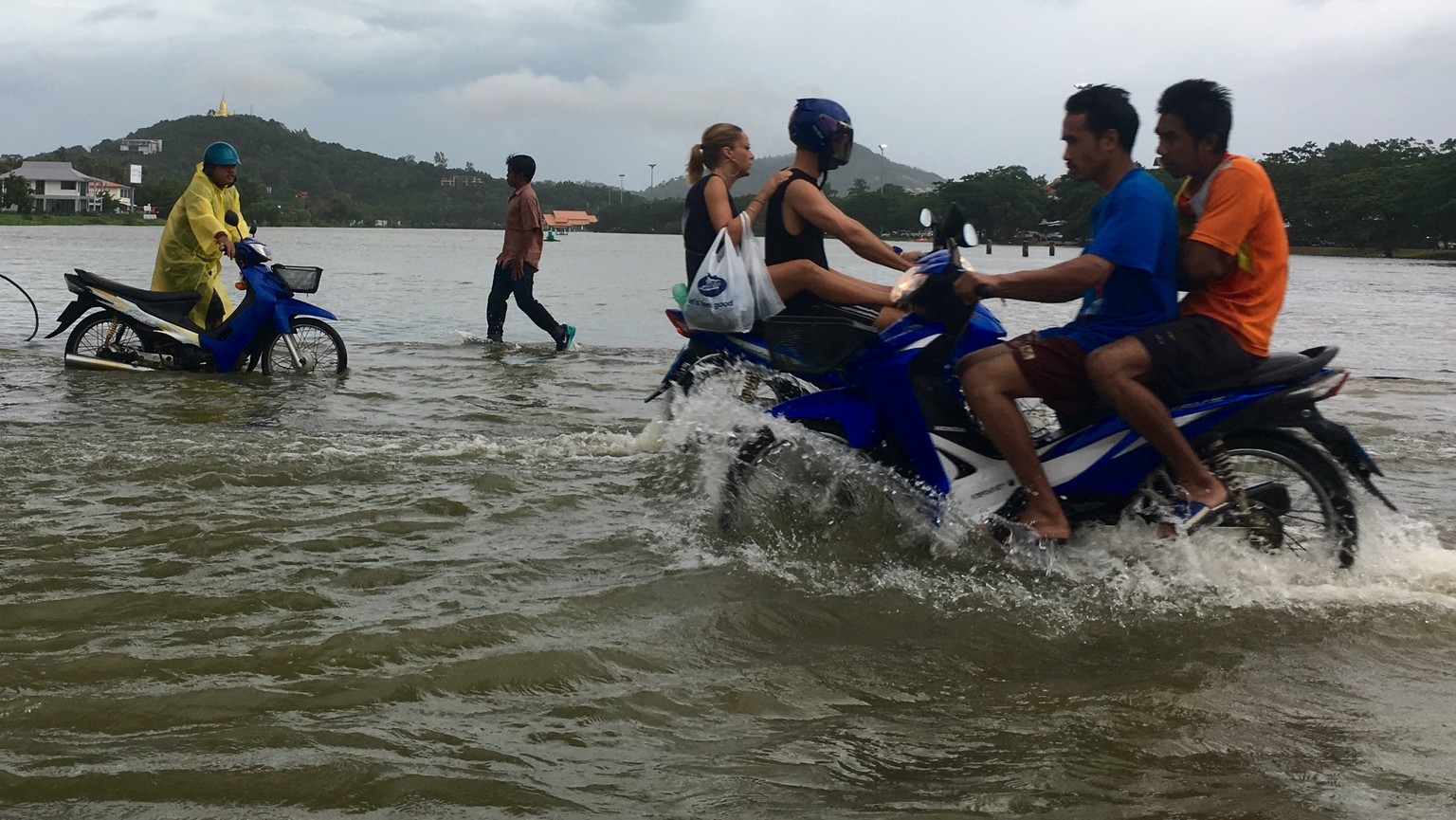 Riders use a road flooded by an overflowing lake on Ko Samui, Thailand Thursday, Jan. 5, 2017. Heavy rains battering parts of Thailand are causing localized flooding on the resort island during a peak ...