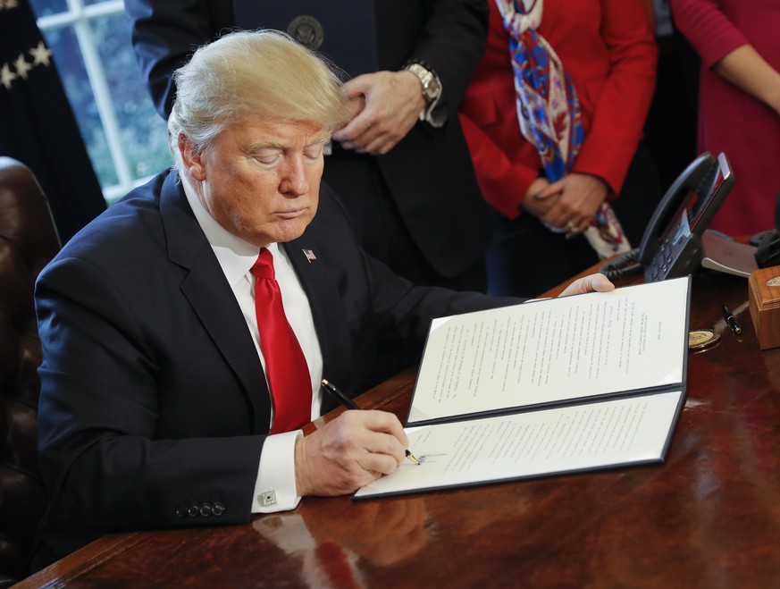 President Donald Trump signs an executive order in the Oval Office of the White House in Washington, Friday, Feb. 3, 2017. Trump signed an executive order that will direct the Treasury secretary to re ...