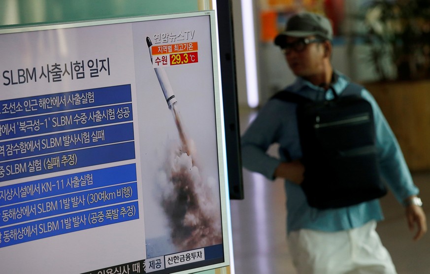 A passenger walks past a TV screen broadcasting a news report on North Korea&#039;s submarine-launched ballistic missile fired from North Korea&#039;s east coast port of Sinpo, at a railway station in ...