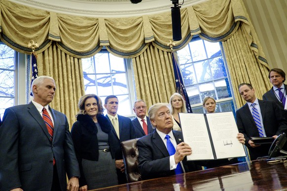 epa05758015 US President Donald J. Trump(C) holds up one of the executive actions that he signed in the Oval Office in Washington, DC, USA, 28 January 2017. The orders outline a reorganization of the  ...