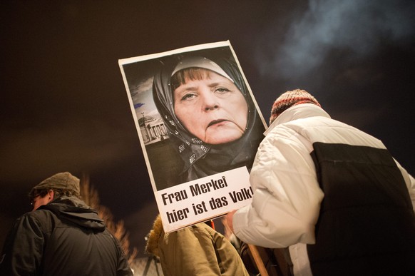 epa04557326 A participant in a rally with the Anti-Islamic Pegida (Patriotic Europeans against the Islamization of the West) movement holds up a picture of Chancellor Merkel wearing a headscarf writte ...