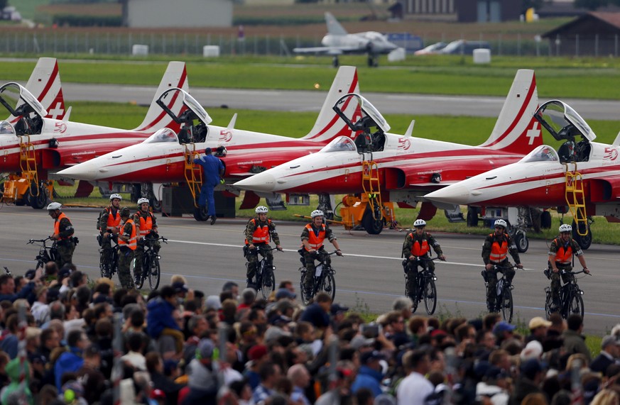 Swiss soldiers cycle in front Northrop F-5E Tigers aircrafts of the Patrouille Suisse during the Air14 airshow at the airport in Payerne August 31, 2014. The Swiss Air Force celebrates their 100th ann ...