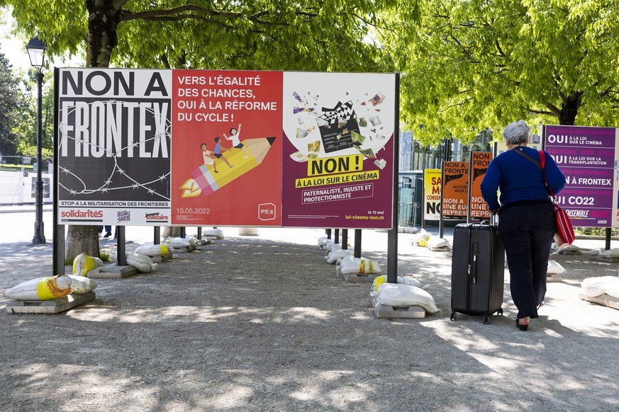 Une personne passe entre les affiches des partis politiques et des associations donnant leurs mots d&#039;ordre pour les votations federales et cantonales du 15 mai, ce mardi 10 mai 2022 a Geneve. Les ...