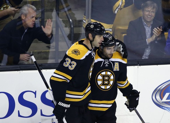 Fans react as Boston Bruins center Patrice Bergeron, right, is congratulated by teammate Zdeno Chara (33) after his goal against the New York Islanders in the first period of an NHL preseason hockey g ...