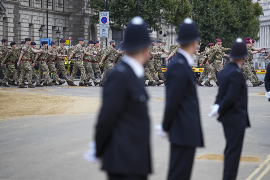 Police watch as armed forces personnel march into position along the route that the coffin of Queen Elizabeth II will be pulled on a gun carriage during her funeral service in Westminster Abbey in cen ...