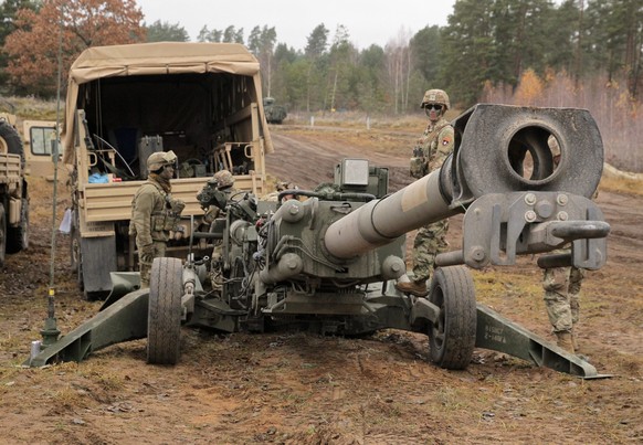 epa09572577 Soldiers stand near a US Army M777 howitzer during exercises of the NATO Battalion Combat Group at the Orzysz training ground, northeastern Poland, 09 November 2021. Soldiers trained in co ...