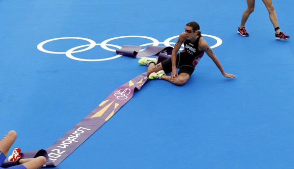 epa03339796 Nicola Spirig of Switzerland sits on the Olympic rings caught in the finish line tape as Lisa Norden of Sweden (L who won silver) collapses and Erin Densham of Australia (bronze,R) slows t ...