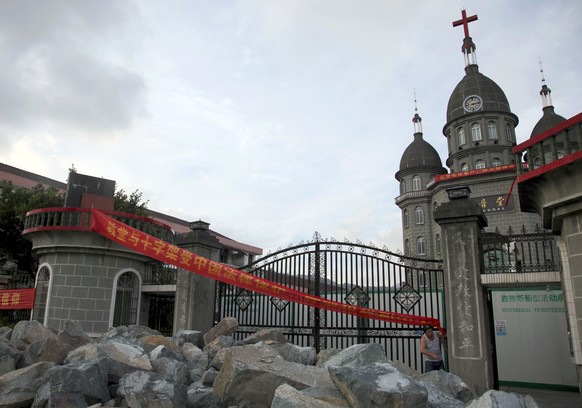 In this photo taken July 16, 2014, a church member of Zengshan Village Christian Church stands near rocks piled up in front of the gate to prevent government workers from moving in equipment to demoli ...