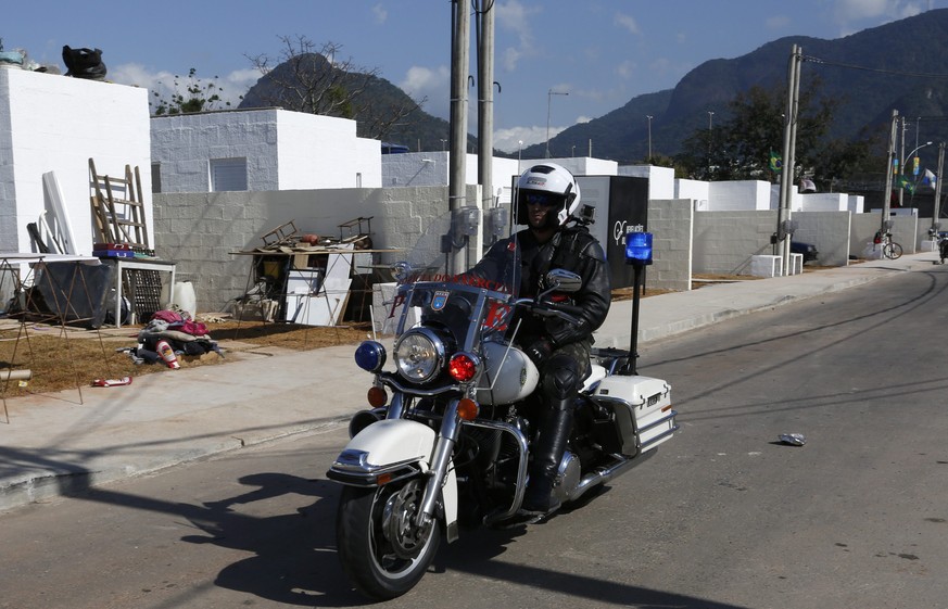 epa05452535 A policeman on motorcycle drives through the new street as people move their possessions in to new homes in the shadow of Olympic Park buildings at Vila Autodromo only three days before th ...