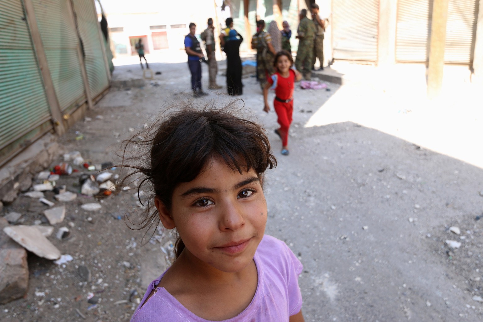 A girl stands near Syria Democratic Forces (SDF) fighters on a damaged street in Manbij, in Aleppo Governorate, Syria, August 7, 2016. REUTERS/Rodi Said