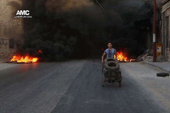 This Sunday, July. 31, 2016 photo, provided by the Syrian anti-government activist group Aleppo Media Center (AMC), shows a Syrian young man burns tyres in an attempt to prevent airstrikes above Alepp ...