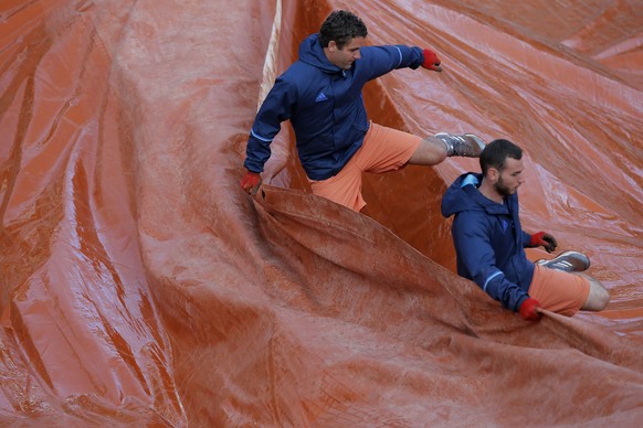 Stadium employees set up a protective canvas on the court as Timea Bacsinszky of Switzerland plays France&#039;s Kristina Mladenovic during their quarterfinal match of the French Open tennis tournamen ...