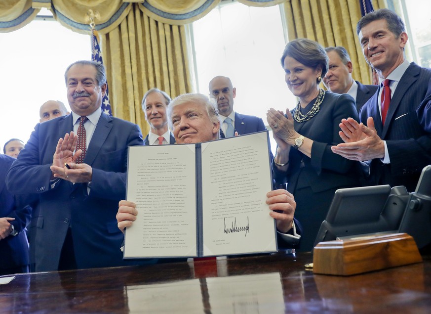 President Donald Trump holds up an executive order after signing it in the Oval Office of the White House in Washington, Friday, Feb. 24, 2017. Dow Chemical President, Chairman and CEO Andrew Liveris  ...
