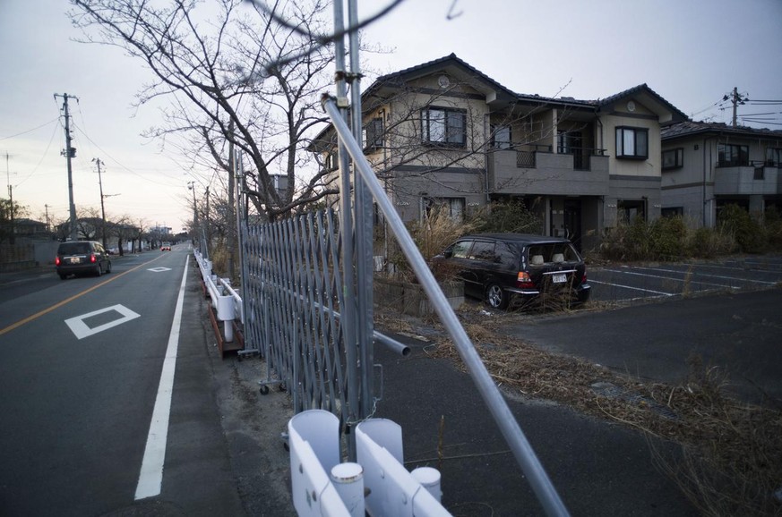 A vehicle, left, moves past another, right, with its rear window broken parked at a deserted apartment complex in a closed residential area in Tomioka town, Fukushima prefecture, northeastern Japan, F ...