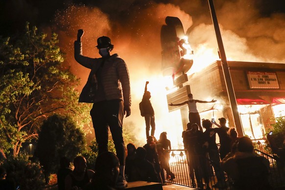 Protestors demonstrate outside of a burning fast food restaurant, Friday, May 29, 2020, in Minneapolis. Protests over the death of George Floyd, a black man who died in police custody Monday, broke ou ...