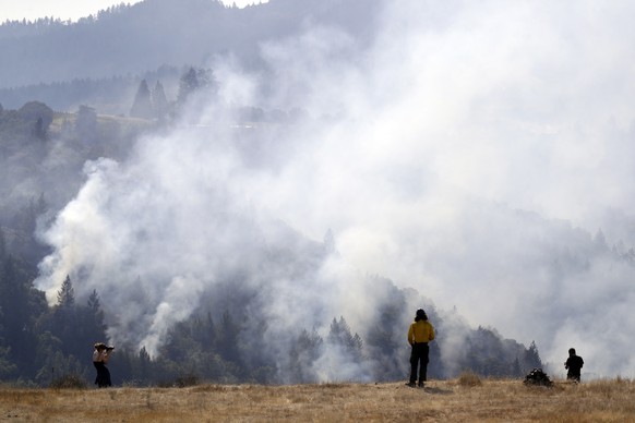 A firefighter, center, and two onlookers watch a smoldering wildfire from a hilltop, Sunday, Oct. 15, 2017, in Oakville, Calif. With the winds dying down, fire officials in California say they are fin ...