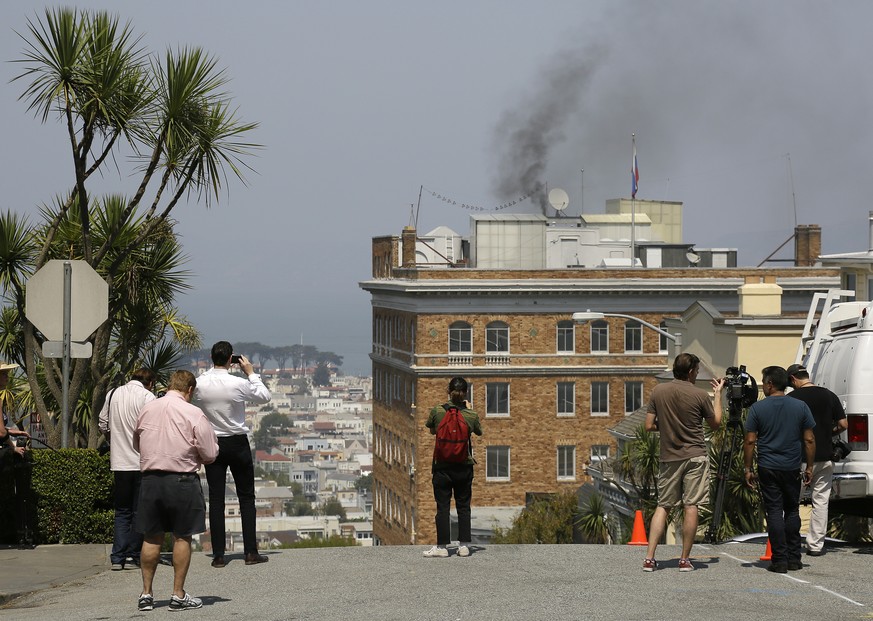 People stop to watch black smoke coming from the roof of the Consulate-General of Russia Friday, Sept. 1, 2017, in San Francisco. The San Francisco Fire Department says acrid, black smoke seen pouring ...