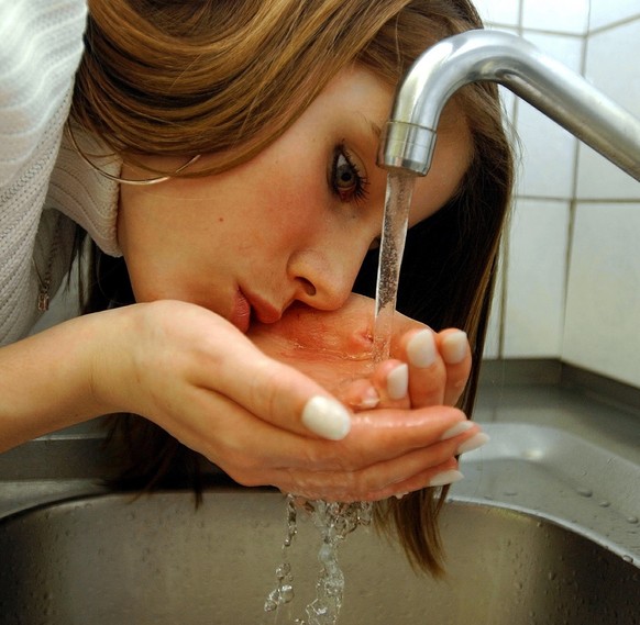 Eine junge Frau genehmigt sich einen Schluck Wasser aus dem Wasserhahn, aufgenommen in einer Kueche in Zuerich am 22. Maerz 2004. Schweizer Trinkwasser ist laut dem Zuercher Kantonslabor jedem Mineral ...