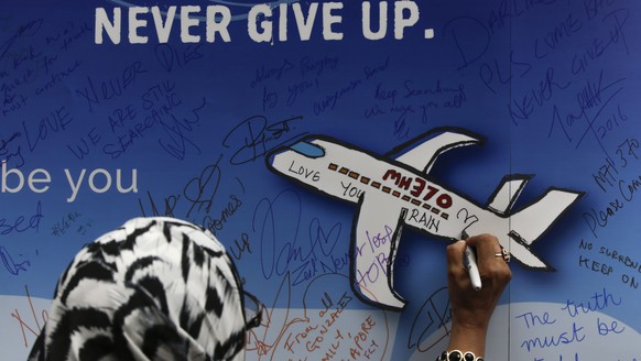 epa05682982 (FILE) A file picture dated 06 March 2016 shows a woman writing messages for the passengers of missing Malaysia Airlines flight MH370 on a banner during a remembrance ceremony to mark the  ...