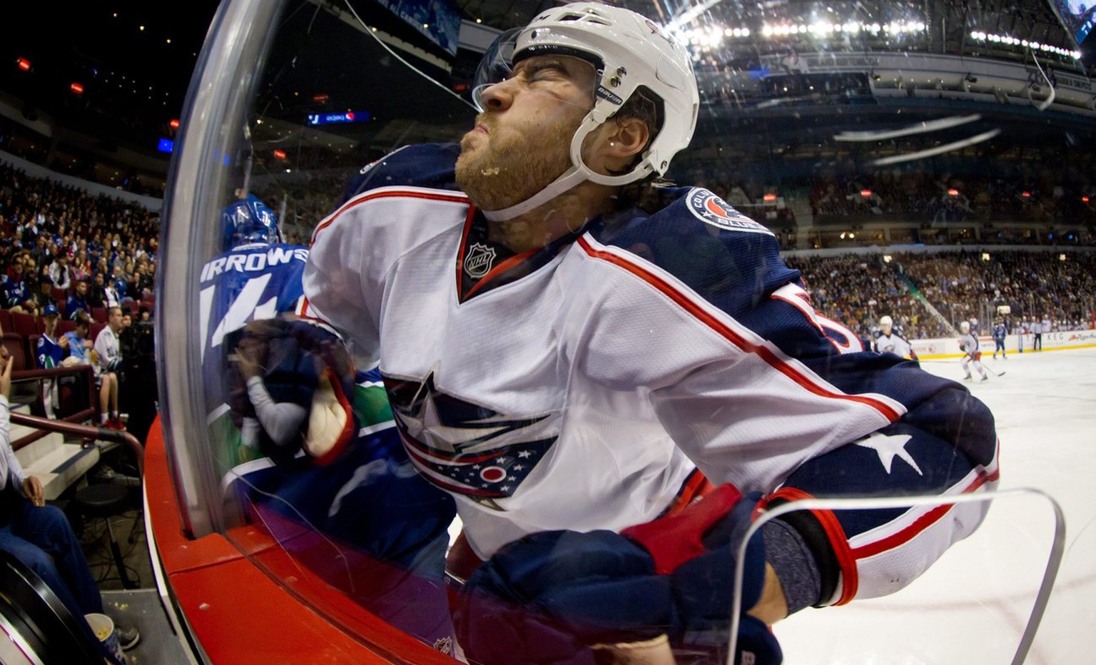 In this photo taken with a fisheye lens, Columbus Blue Jackets&#039; David Savard, right, crashes into the glass after missing a check on Vancouver Canucks&#039; Alex Burrows, left, during first-perio ...