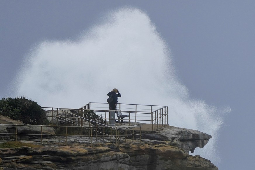 People stand on a rock ledge as huge swells hit the headland at Bondi Beach in Sydney, Australia, Sunday, July 3, 2022. A severe weather warning for heavy rainfall and strong winds has been issued for ...