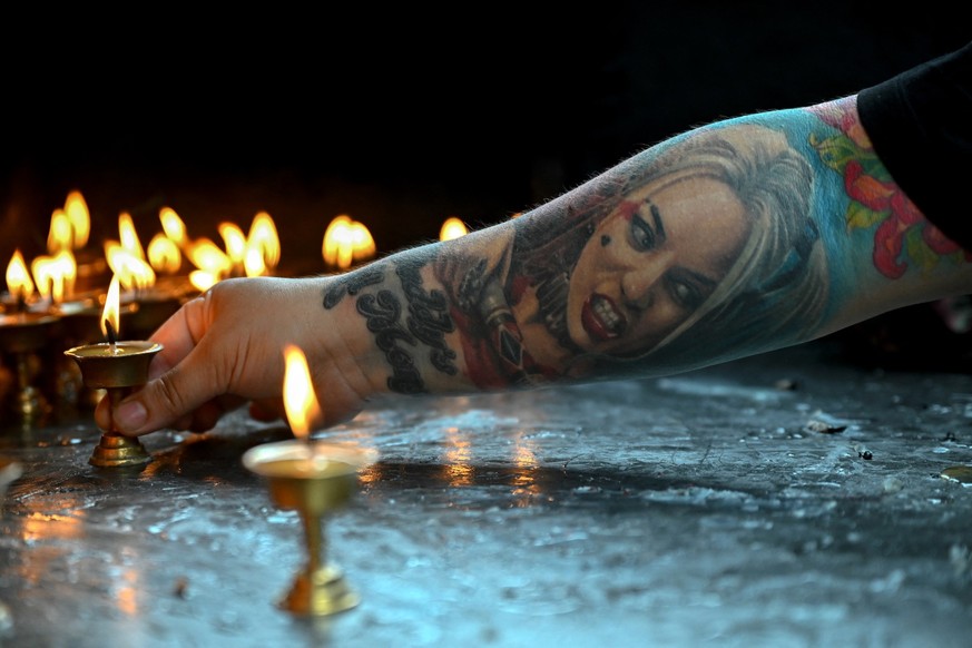 A woman with a tattoo of the Harley Quinn character from the Suicide Squad movies lights an oil lamp inside a temple at the Durbar Square in Kathmandu on September 13, 2025. Nepal&#039;s former chief  ...