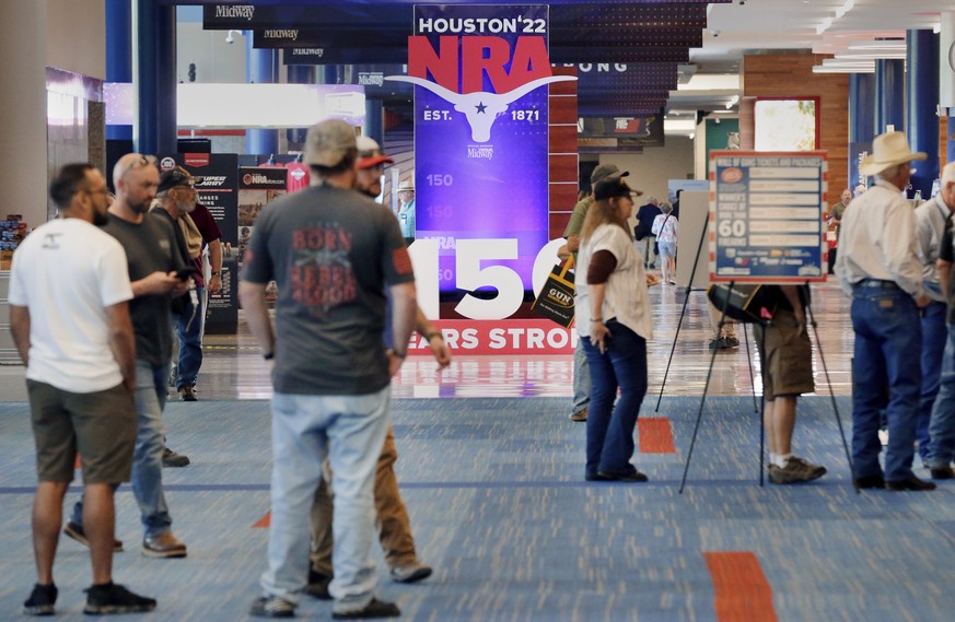 People gather at booths near some of the signage in the hallways outside of the exhibit halls at the NRA Annual Meeting held at the George R. Brown Convention Center Thursday, May 26, 2022, in Houston ...