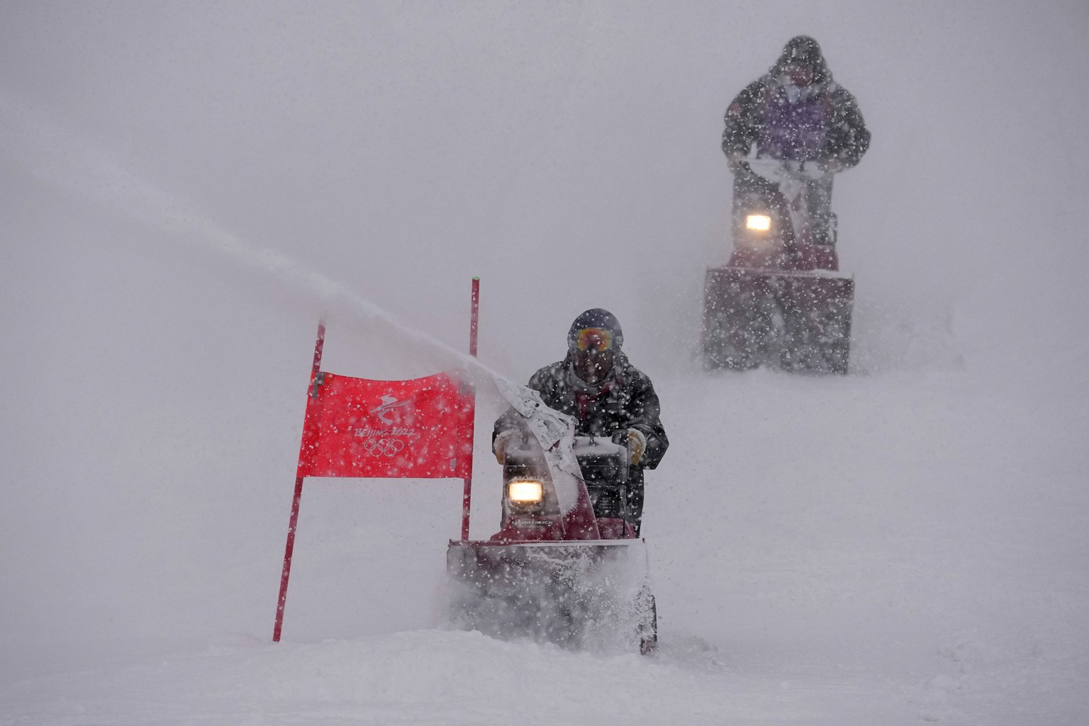 Course workers blow snow from the men's giant slalom course as the snow comes down at the alpine ski venue at the 2022 Winter Olympics, Sunday, Feb. 13, 2022, in the Yanqing district of Beijing. ...