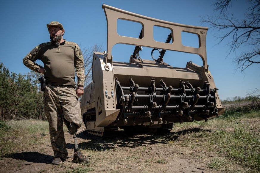 Andriy Ilkiv, chef du département de neutralisation des explosifs et munitions de la police nationale de a région de Lviv, montre sa prothèse de jambe, avec en fond un engin de déminage GCS-200.