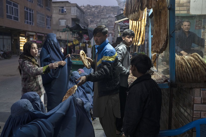 FILE - A man distributes bread to Burka-wearing Afghan women outside a bakery in Kabul, Afghanistan, Thursday, Dec, 2, 2021. Pakistan is rallying Muslim countries to help Afghanistan stave off an econ ...