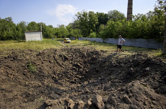 epa10056611 A man stands next to a shell crater outside a school for visually impaired children, following a Russian rocket strike on Kharkiv, Ukraine, 07 July 2022. Kharkiv and surrounding areas have ...