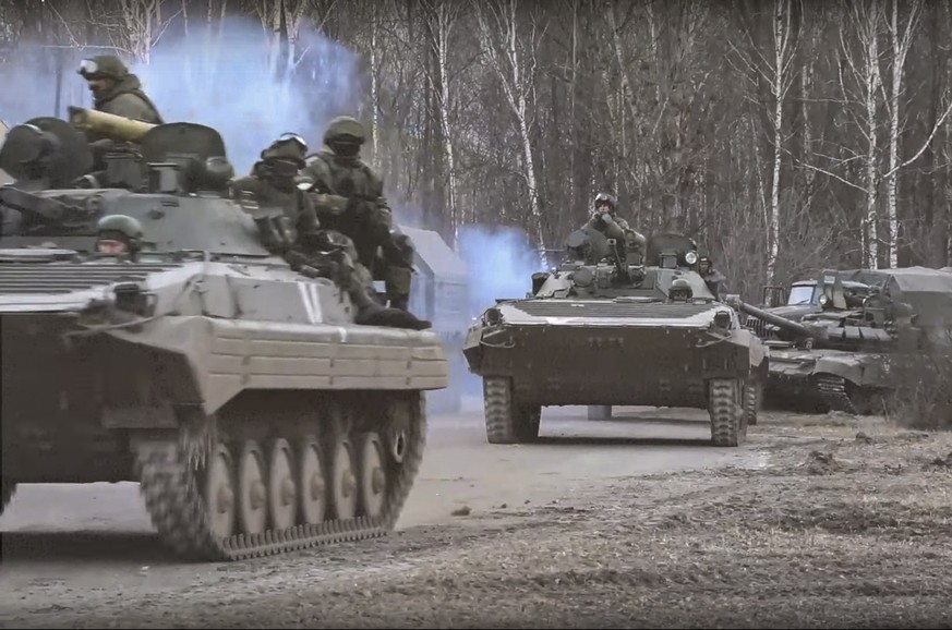 epa09807293 A still image taken from a handout video made available by the Russian Defence Ministry press service shows Russian servicemen drive on armoured military vehicle on the road near Kyiv (Kie ...