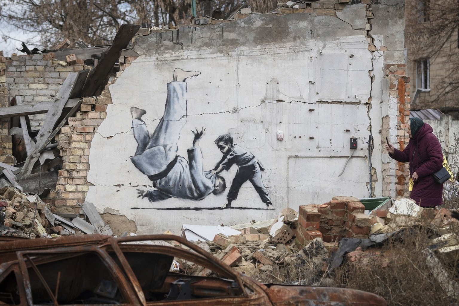 A woman takes a picture of artwork that might have been made by British street artist Banksy on a building destroyed by fighting in Borodyanka, in the Kyiv region, Ukraine, Sunday, Nov. 13, 2022. (AP ...