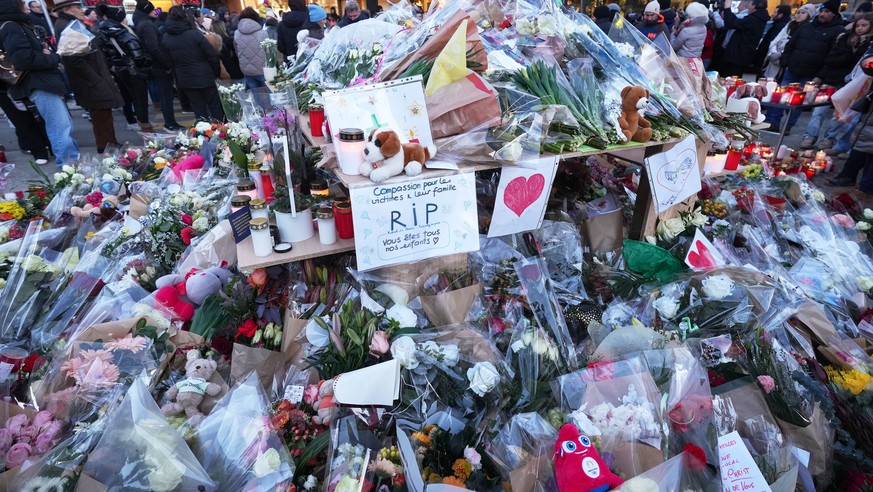 FILE - People stand around floral tributes and candles placed outside the sealed off Le Constellation bar in Crans-Montana, Swiss Alps, Switzerland, on Jan. 3, 2026, where a devastating fire left dead ...