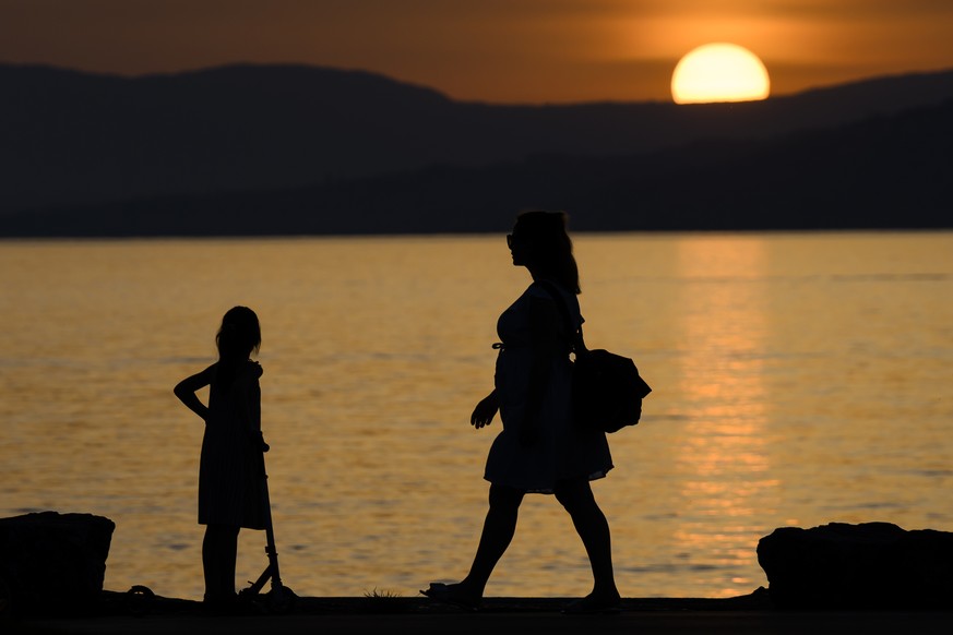 Une femme et un enfant regardent le soleil qui se couche derriere le Jura au bord du lac Leman le vendredi 17 juin 2022 a Villeneuve. La chaleur sera dangereuse pour la sante a l&#039;approche du week ...