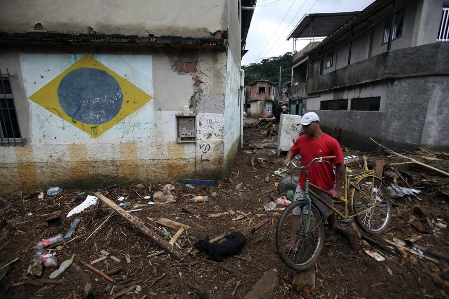 epa03523444 A man carries a bicycle in a street after a flood due to heavy rain in Duque de Caxias near Rio de Janeiro, Brazil, 03 January 2013. At least one person died from the flood, according offi ...