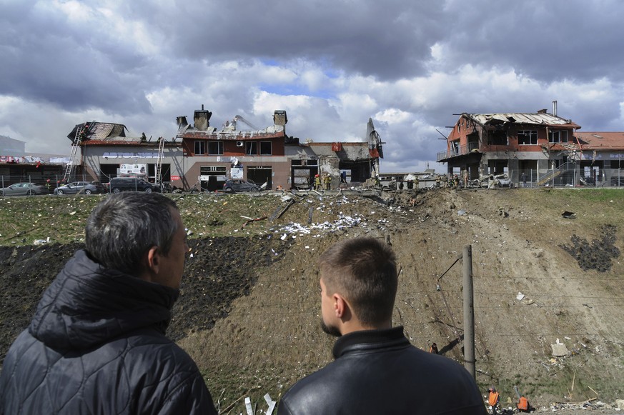 Men look on as firefighters work to extinguish a fire after an airstrike hit a tire shop in Lviv, Ukraine, Monday, April 18, 2022. Russian missiles hit the city of Lviv in western Ukraine on Monday, k ...