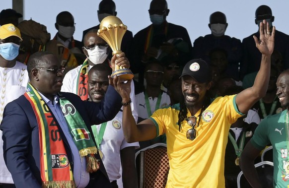 Senegal's President Macky Sall, left, and coach Aliou Cisse, right, hold the trophy during a ceremony after the national football team arrived back at the airport in Dakar, Senegal Monday, Feb. 7 ...
