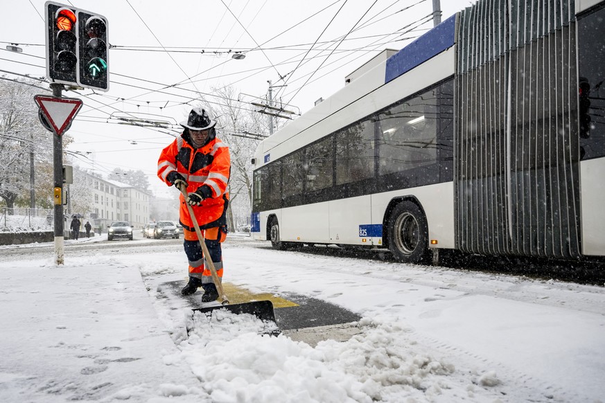 Un employe de la voirie de la ville de Lausanne enleve la neige sur la chaussee avec une pelle devant un bus des TL lors des chutes de neige le jeudi 21 novembre 2024 a Lausanne. (KEYSTONE/Jean-Christ ...